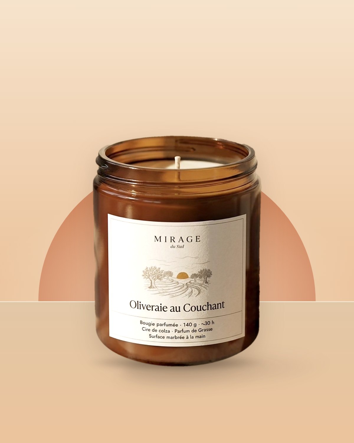 Bougie Oliveraie au Couchant de Mirage du Sud : pot en verre ambré, étiquette crème illustrée d'oliviers au soleil couchant, devant un soleil orangé stylisé