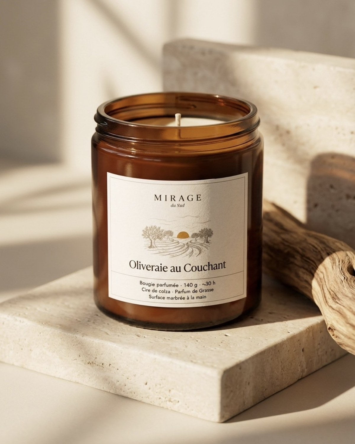 Bougie Oliveraie au Couchant posée sur une plaque de travertin, à côté d'un morceau de bois flotté, dans la lumière chaude du soir